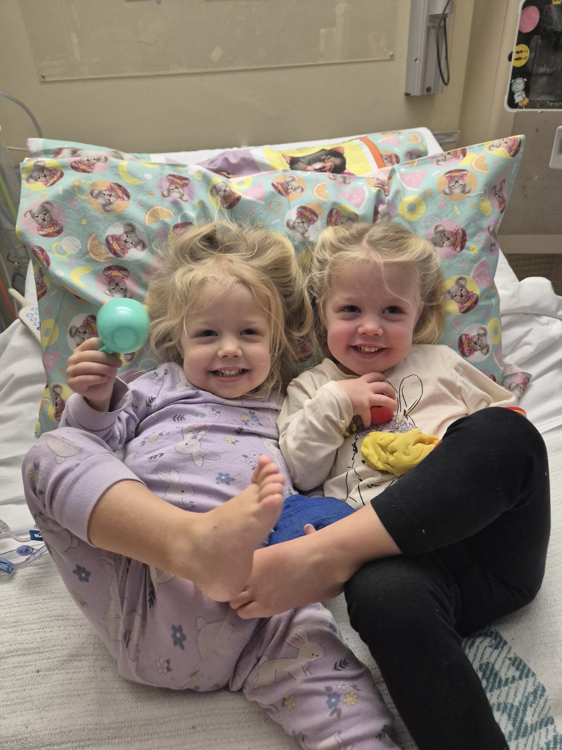 Smiling twins supported by Ronald McDonald House Charities Greater Western Sydney in a hospital bed