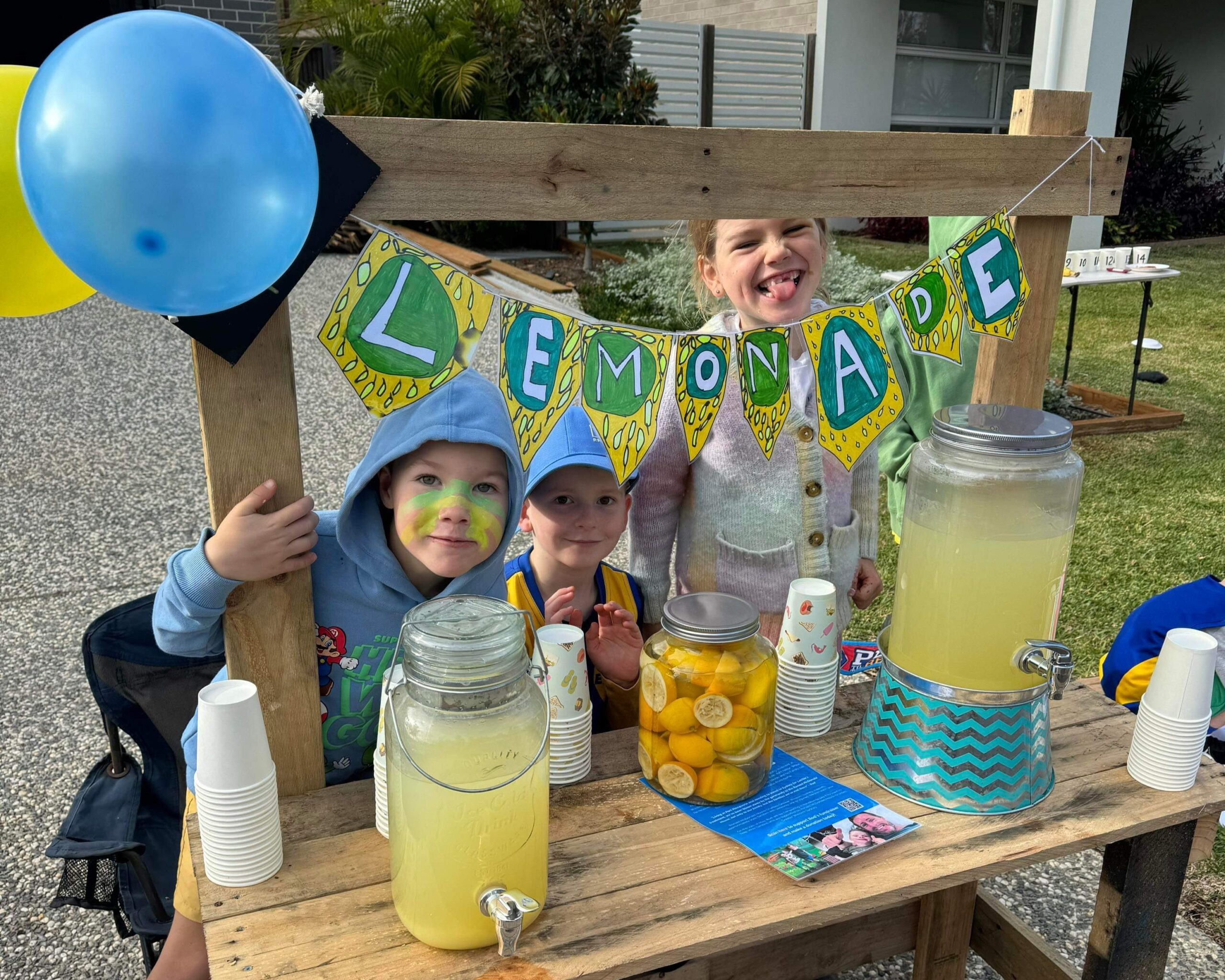 Three children at a lemonade stand, getting involved and supporting their father running a marathon to fundraise for Ronald McDonald House Charities Greater Western Sydney